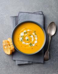 Pumpkin, carrot cream soup in a bowl. Grey background. Top view.