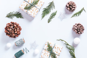 Stylish white and green Christmas flat lay with huge pine cones, cedar branches, presents and decorations. Frame with Christmas ornaments and natural elements