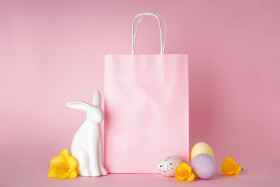 Easter bunny and colored Easter eggs with paper bag on pink background, place for text. Happy Easter concept.