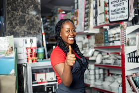 Positive dark skinned female sale girl posing proudly in cosmetic supermarket given a thumbs up