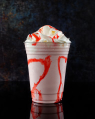 Strawberry milkshake with strawberry syrup in clear glass on dark background.